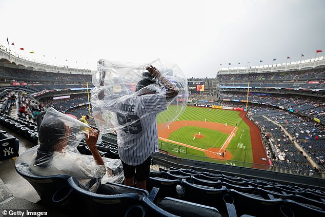 A fan wearing an Aaron Judge jersey scrambles to pull on a poncho as the rain begins to fall