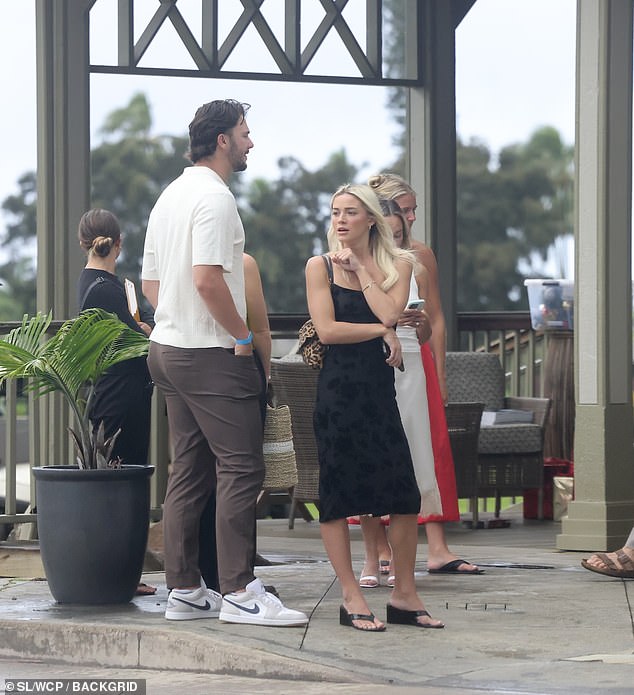 She Was Wearing A Stylish Black Dress And Matching Shoes, While Skenes Pulled On A Casual White T-Shirt, Brown Pants And White Nike Sneakers